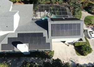 Aerial view of a house with solar panels installed on the roof and a screened-in pool area, with a driveway and a white car parked outside.